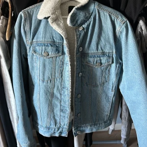 Ljusblå jeansjacka med teddyfoder från Bik Bok - Säljer en snygg ljusblå jeansjacka från Bik Bok med mysigt vitt teddyfoder. Jackan har knappar framtill och två bröstfickor med knappstängning. Perfekt för kyligare dagar!
