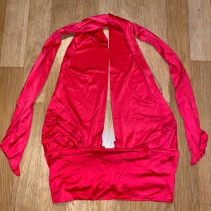 Röd ärmlös topp - Snygg röd ärmlös topp med djup urringning och knytband. Perfekt för en kväll ute eller en festlig tillställning. Tillverkad i ett glansigt material som ger en lyxig känsla.