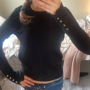 Svart tröja från Zara med knappar - Säljer en stilren svart tröja från Zara med långa ärmar och dekorativa knappar vid ärmsluten. Perfekt för en elegant look. Tröjan är mjuk och bekväm att bära. Orginal pris 329💕💕