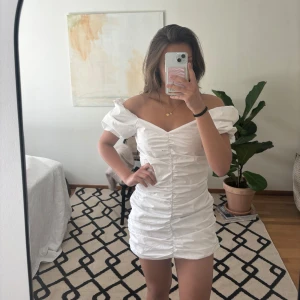 Vit kort klänning med puffärmar - Säljer en stilren vit kort klänning med puffiga axelbandslösa ärmar och rynkdetaljer framtill. Perfekt för sommarens alla tillfällen. Klänningen har en smickrande passform och en v-ringad design. Perfekt nu till studenten🌸 Aldrig använd, alla lappar finns kvar☺️🌸Sterlek 34, passar mig som brukar ha XS-S🌸