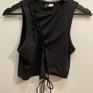 Svart ribbad croppad topp - Svart ribbad croppad topp med snörning framtill. Aldrig använt den 