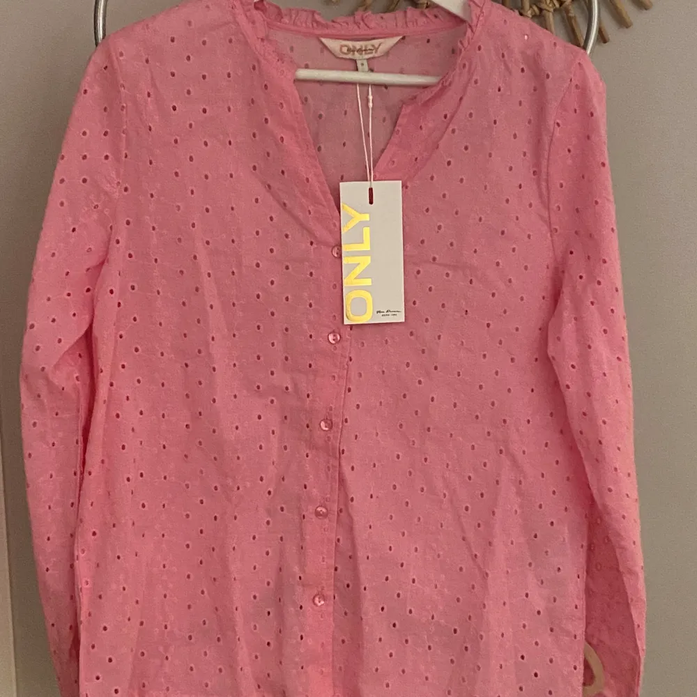 Säljer en söt rosa blus från ONLY med broderade detaljer och knappar framtill. Blusen har långa ärmar och ett diskret prickigt mönster. Perfekt för en fräsch och stilren look.. Paidat.