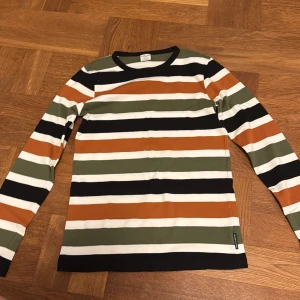 Randig långärmad tröja - Säljer en snygg randig tröja från Polarn O. Pyret i grönt, orange, svart och vitt. Tröjan har långa ärmar och en klassisk rund halsringning. Perfekt för en stilren och bekväm look.