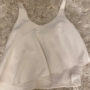 Vit linnetopp från Pull&Bear - Säljer en stilren vit linnetopp från Pull&Bear. Toppen har en asymmetrisk design med dubbla lager och tunna axelband. Perfekt för varma dagar eller som en del av en lager-på-lager-look. 🕊️