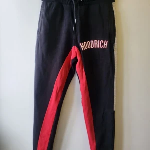 Hoodrich byxor - Snygga svarta mjukisbyxor från Hoodrich med röda och vita detaljer. Byxorna har snörning i midjan och en avslappnad passform. Perfekta för en casual look.