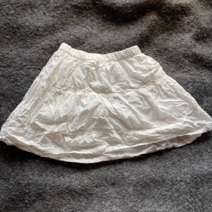 Vit sommar kjol från H&M - Säljer en söt vit kjol från H&M med elastisk midja. Kjolen har en lätt volangdetalj och är perfekt för varma dagar. Den är gjord i ett mjukt och bekvämt material. Perfekt till sommaren ! Säljer pga att den inte passar mig längre
