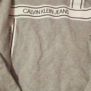 Grå tröja från Calvin Klein Jeans och svart hoodie från EA7 - Säljer en stilren grå tröja från Calvin Klein Jeans med logga över bröstet och en svart hoodie från EA7 med dragkedja och logga på bröstet. Perfekta för en casual look. Hör av dig vid intresse! 150kr Calvin Klein 200 Armani i kl Gant tshirt på köpet 