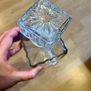 Elegant fyrkantig glas tillbringa i glas - Säljer en elegant glas tillbringa i klart glas med fyrkantig form och dekorativt mönster. Flaskan har en matchande fyrkantig kork med stjärnmönster på toppen. Perfekt för att förvara din favoritparfym eller som en stilren inredningsdetalj.