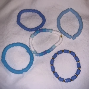 Färgglada armband i blå och vita nyanser - Säljer ett set med fem elastiska armband i olika blå och vita nyanser. Ett av armbanden har små guldfärgade detaljer som ger en extra touch. Perfekt för att liva upp din outfit! De kostar 25st