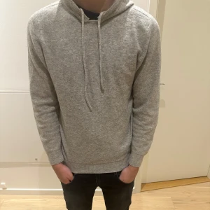 Merinoull hoodie - Säljer en stilren grå hoodie. Tröjan har långa ärmar och ribbade muddar vid ärmslut och nederkant. Perfekt för en avslappnad look. Storlek M, Merinoull