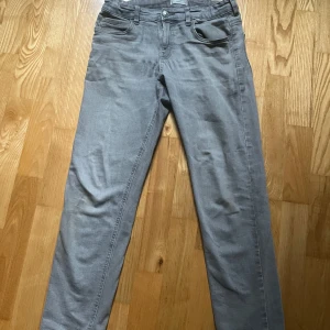 Grå byxor från MNG - Säljer ett par stilrena grå byxor från MNG. De har en klassisk design med fem fickor och knappgylf. Perfekta för en avslappnad look.