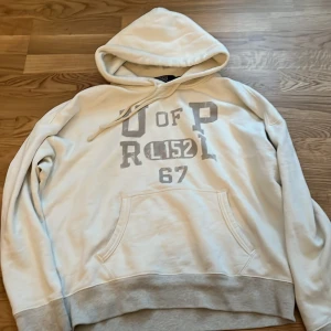 Vit hoodie från Polo by Ralph Lauren - Säljer en vit hoodie från Polo by Ralph Lauren med tryck på framsidan. Den har en klassisk känguruficka och justerbar huva med snören. Perfekt för en avslappnad stil. Den är i väldigt fint skick och har andvönts sparsamt, kom med frågor och funderingar.