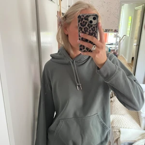 Grön hoodie med ficka framtill - Säljer en enkel och stilren grå hoodie med luva och dragsko. Tröjan har en stor magficka och långa ärmar, perfekt för en avslappnad look. Passar till det mesta och är superbekväm. Endast använd 2 ggr