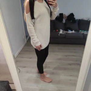 Vit ribbad offshoulder-tröja med svarta band - Säljer en vit ribbad tröja med offshoulder-design och svarta band vid axlarna. Tröjan har lång ärm och en avslappnad passform, perfekt för dig som gillar en unik och trendig stil.