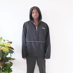 Svart vindjacka med huva från Claas - Svart vindjacka från Claas med huva och halv dragkedja framtill. Jackan har en diskret vit linje över bröstet och elastiska muddar vid ärmsluten. Perfekt för blåsiga dagar och enkel att matcha med det mesta.  Size M  Length:73cm Chest:64cm   Feel free to ask any question