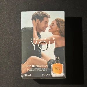 Emporio Armani Stronger With You Eau de Toilette 100ml - Emporio Armani Stronger With You är en herrparfym i en elegant 100ml flaska. Doften är modern och maskulin, perfekt för dig som vill sticka ut. Förpackningen har en stilren design med en bild på ett par och parfymflaskan i hörnet.