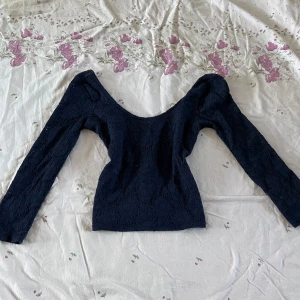 Svart spets topp - Säljer en svart topp i spets med lång ärm och djup urringning. Blusen har en figurnära passform och är tillverkad i ett vackert spetsmaterial som ger en elegant känsla.🌸🌷