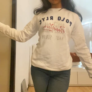 Vit långärmad tröja från Polo Ralph Lauren - Säljer en vit långärmad tröja från Polo Ralph Lauren med tryckt text i blått och rött framtill. Klassisk och enkel design med rund halsringning. Perfekt till jeans eller kjol. Storleken är M men passar mig perfekt som är vanligtvis XS eller S