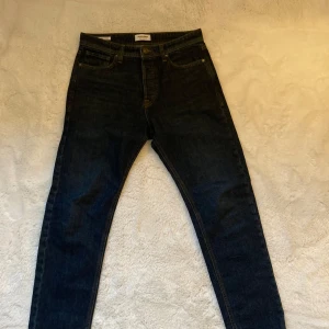Mörkblå jeansbyxor från Jack & Jones - Säljer ett par mörkblå jeans från Jack & Jones, modell Relaxed Chris. Klassisk femficksdesign med raka ben och normal passform. Jeansen har tydliga kontrastsömmar och stängs med knappar.