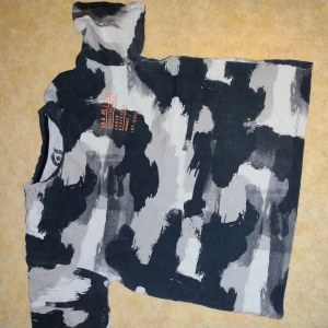 Svart och grå camo t-shirt - Cool t-shirt med svart, grått och vitt camouflagemönster. Tryck i orange framtill och rund hals. Perfekt för dig som gillar streetstyle och vill sticka ut lite extra.