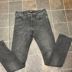 Svarta jeans från Jack & Jones - Säljer ett par svarta jeans från Jack & Jones med klassisk femficksdesign och knappgylf. Jeansen har en rak passform och är tillverkade i ett stretchigt denimtyg som ger bra komfort. Perfekta till vardags och enkla att matcha med olika stilar.