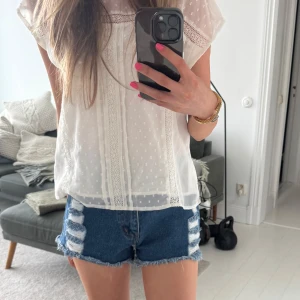 Blå jeansshorts med slitningar - Säljer ett par blå jeansshorts med råa kanter och slitna detaljer framtill och baktill. Shortsen har klassisk femficksdesign, hög midja och fransig nederkant💓 mått finns på bilderna!