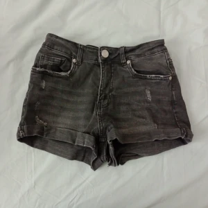 Svarta jeansshorts - Snygga svarta jeansshorts från FB Sister i storlek XS. Modellen har klassisk femficksdesign, uppvikta benslut och slitna detaljer framtill. Perfekta för varma dagar och enkel att matcha med olika toppar.