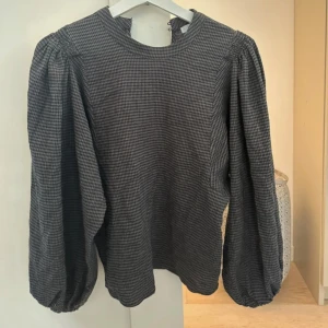 Grå rutig blus med puffärmar - Säljer en grå rutig blus med rund halsringning och långa puffärmar. Blusen har ett diskret rutmönster och är perfekt för dig som gillar en stilren men ändå trendig look. 