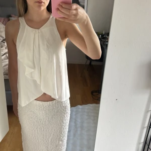 Vit ärmlös blus från Zara - Säljer en vit ärmlös blus från Zara i storlek XS. Blusen har en snygg omlott-detalj framtill och ett lätt, luftigt material som passar perfekt till sommaren. Stängs med knapp i nacken.