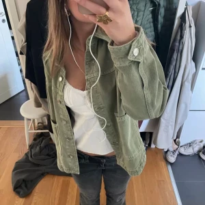 Jeansjacka - Säljer olivgrln jeansjacka med stora fickor framtill och knappar längs hela framsidan. Jackan har en avslappnad passform och är perfekt att slänga över en t-shirt eller linne.