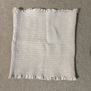 Beige smockad tubtopp från H&M - Säljer en beige smockad tubtopp från H&M med volangdetaljer upptill och nedtill. Perfekt att styla till sommaren för en enkel och trendig look.