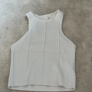 Vit ribbad linnetopp - Säljer en vit ribbad linnetopp med hög halsringning och ärmlös design. Toppen har en croppad passform och är perfekt för varma dagar. Enkel och stilren modell som passar till mycket.