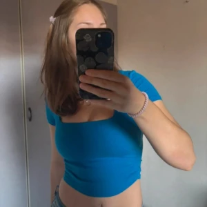 Blå croppad topp från Zara - Säljer en blå croppad topp från Zara med fyrkantig ringning och korta ärmar. Toppen har rynkade sidor som ger en snygg detalj. Perfekt till jeans eller kjol! Den har ett litet hål (se bild) men man lägger inget märket i det, syns knappt.☺️💕