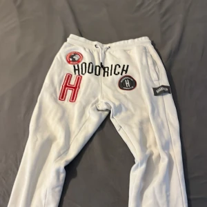 Vita mjukisbyxor från Hoodrich med patch-detaljer - Säljer ett par vita mjukisbyxor från Hoodrich med flera broderade patchar och loggor framtill. Byxorna har dragsko i midjan och är tillverkade i mjukt material. Perfekta för en avslappnad stil.