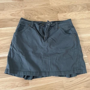 Mörkgrå jeans minikjol från Jones & Co - Säljer en mörkgrå minikjol från Jones & Co med fickor fram och bak samt knapp- och dragkedjestängning. Kjolen har coola detaljer med sömmar och slitsar baktill. Perfekt för en avslappnad och trendig look. Passar mig som brukar ha storlek S/M i underdelar. 