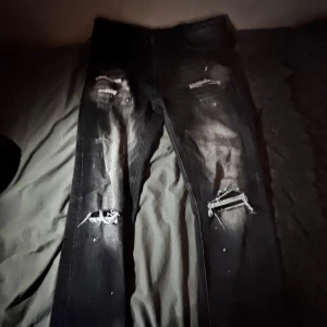 Svarta distressed jeans från Supply & Demand - Säljer ett par svarta jeans från Supply & Demand med slitna detaljer och hål på knäna. Jeansen har normal passform och klassisk femficksdesign. Midjemått 34W. Perfekta för en edgy streetstil.
