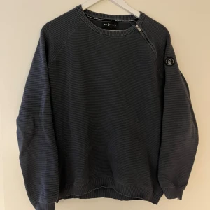 Mörkblå stickad tröja från Sail racing - Säljer en mörkblå stickad tröja från sail racing med rund halsringning och dragkedjedetalj vid axeln. Tröjan har långa ärmar och ribbade muddar. Klassisk patch på ena ärmen.