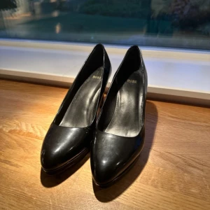 Hugo Boss högklackade skor  - Klassiska svarta högklackade skor från Hugo BOSS med rund tå som är skinlackade. Använda ett fåtal gånger.  Nypris ca 3000kr. 