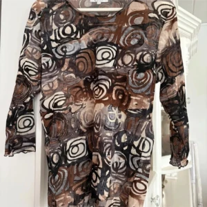 Mönstrad topp från Signature Experience - Säljer en långärmad topp från Signature Experience i storlek L. Toppen har ett abstrakt mönster i bruna, svarta, grå och beige toner. Materialet känns mjukt och stretchigt, perfekt för dig som gillar unika prints.