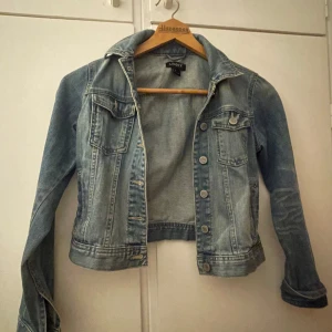  jeansjacka  - Säljer en klassisk ljusblå jeansjacka från Lindex. Jackan har knappar framtill, två bröstfickor med lock och knapp storlek 34