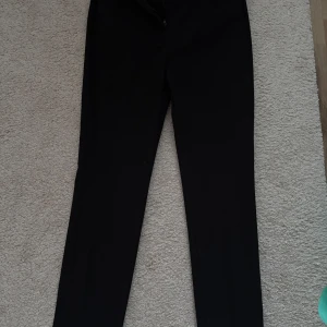 Svarta kostymbyxor från Zara - Svarta kostymbyxor från Zara med normal passform. Byxorna har dragkedja och knapp framtill samt diskreta fickor. Perfekta till en stilren look och enkla att matcha med olika toppar.