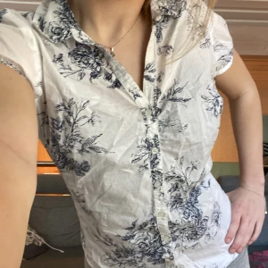 Vit blommig kortärmad skjorta från KappAhl - Säljer en vit skjorta från KappAhl med blått blommigt mönster. Skjortan har korta ärmar, klassisk krage och knäppning framtill. Perfekt för en fräsch och somrig look! Passar mig som vanligt vis har 34/36 i överdelar trots att den är i 42💕