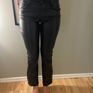 Svarta skinnbyxor med raka ben - Snygga svarta skinnbyxor med normal passform och lite utbredda längst ner. Byxorna har klassisk femficksdesign, bälteshällor och stängs med dragkedja och knapp. Perfekta för en trendig och härlig look.