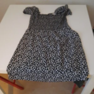 Svart blommig klänning med puffärm - Söt svart klänning med vita små blommor och korta puffärmar. Klänningen har en rak passform och fyrkantig ringning, perfekt för en trendig och avslappnad look.