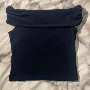 Mörkblå offshoulder topp från Gina Tricot - Säljer en mörkblå offshoulder topp från Gina Tricot. Toppen har en bred, vikt kant över axlarna och är ärmlös. Perfekt för en trendig och stilren look. Materialet känns mjukt och stretchigt.