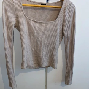  Gina tricot Beige ribbad långärmad topp med fyrkantig ringning - Säljer en beige ribbad topp med lång ärm och snygg fyrkantig ringning. Perfekt att styla med jeans eller kjol för en enkel men trendig look. Mjuk och stretchig i materialet. Använd få tal gånger men som perfekt skick 😼🩷 