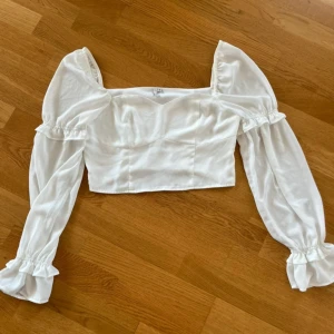 Vit blus med puffärmar från NLY Trend - Säljer en vit blus från NLY Trend med långa, transparenta puffärmar och volangdetaljer vid ärmslut och axlar. Blusen har en croppad passform och fyrkantig ringning. Säljer pga kommer inte till användning. 