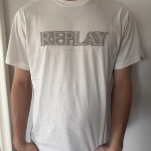 Vit t-shirt från Replay - Säljer en vit t-shirt från Replay med grå logotyp tryckt på bröstet. Klassisk passform och rund halsringning. Perfekt för dig som gillar stilrena och enkla plagg. Helt ny