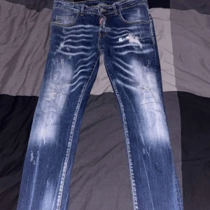 Dsquared2 blå jeans - Säljer ett par blå jeans från dsquared2. Klassisk femficksmodell med gylf och knapp, samt Dsquared2-logga vid fickan. Snygga kontrastsömmar och rak passform.