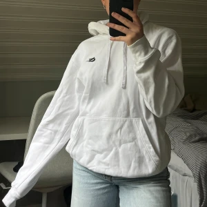 Vit hoodie från Nike - Säljer en klassisk vit hoodie från Nike med svart logga på bröstet. Tröjan har huva med snören och en stor magficka🤍